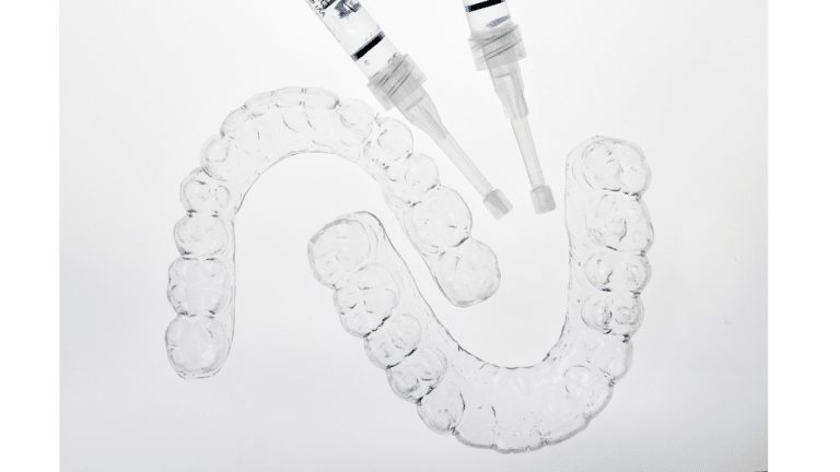 Two clear aligners and two syringes with lighted backdrop